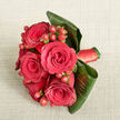 From a high, almost contemplative viewpoint, a richly coloured bouquet of red roses and berries rests on a pale beige, lightly textured fabric that looks like soft linen or finely woven cotton, the sort you might find in a calm Gerrards Cross home overlooking West Common. At the centre of the composition, five to six luxurious red roses sit in close company, each bloom opening fully with a classic spiral heart and densely layered petals that seem to invite a touch. Between the roses, clusters of small, spherical Hypericum berries appear in a brighter red, some with hints of orange-red where the light catches them, bringing a playful yet elegant contrast to the velvety petals. Surrounding this focal cluster, generous dark green tropical leaves are carefully shaped and wrapped, forming a natural collar that both frames the flowers and gives the bouquet a modern, structured silhouette. Their smooth surfaces and gently curling edges create a dynamic interplay of shadow and sheen. The stems below are neatly secured with a matching red satin ribbon, wound tightly so that only a glimpse of its glossy texture is visible, hinting at the care taken in the binding. Soft, diffuse lighting falls evenly across the bouquet, deepening the reds and enriching the greens while maintaining a tranquil, intimate mood, like afternoon light filtering through a window near Gerrards Cross station. The overall effect is one of confident romance and refined celebration, perfect for a bridal bouquet carried at a local church wedding or an anniversary surprise delivered to a favourite restaurant in the village.