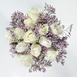 Seen from directly above, this sympathy bouquet takes on the shape of a serene, circular medallion of white and lavender, resting against a bright, uncluttered white background. At the centre, around twelve white roses are closely arranged, each bloom showing its own character. Some are still compact and bud-like, their outer petals wrapped protectively in smooth curves, while others have relaxed into open spirals, revealing delicately layered centres. The colour of the roses is a clear, creamy white, deepening very slightly to pale ivory or the softest yellow at the heart of a few blossoms, giving them a natural, gentle warmth. Interlaced throughout the roses are airy sprays of Limonium, with clusters of tiny lavender-purple flowers that create a fine, clouded texture. This lilac haze wraps around the roses, offering a subtle contrast in both colour and structure, and adding a feeling of lightness and depth to the arrangement. Slender glimpses of green stems and modest foliage peek through here and there, suggesting freshness while keeping the overall look clean and restful. The bouquet feels quiet and dignified, a design that seems made for hushed chapels, reflective services, or private goodbyes. In Gerrards Cross, it is the kind of comforting floral tribute that might be sent to a family home near the station or to a remembrance gathering off Marsham Lane, carrying a message of compassion and peace through its restrained beauty and thoughtful balance of tones.