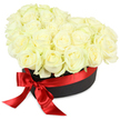 This sumptuous floral gift box, designed for Gerrards Cross residents, features an opulent dome of flawless white roses-freshly cut and skillfully arranged to form a heart-shaped cluster that spills elegantly over the edge of a matte black container. Each rose, ranging from tightly budded to fully open, displays creamy petals highlighted by subtle hints of green found only in the freshest selections from local nurseries. The box itself, chic and sturdy, is dressed with a gleaming red satin ribbon, its luxurious bow set confidently to the front-left, the glossy tails flowing to enhance the feeling of romance and sophistication. Bright, even lighting accentuates the lush textures, from velvety petal to shimmering ribbon, and brings out the vivid contrast between the radiant blooms and the jet-black box, all set against a clean white background that focuses attention on floral artistry. Crafted by hands familiar with the traditions of Gerrards Cross markets and special gatherings, this arrangement effortlessly conveys pure affection, refined style, and thoughtful remembrance-making it the ideal centerpiece for Valentine's surprises, anniversaries, Mother's Day celebrations, or dignified tributes. The overall impression is one of heartfelt luxury and graceful sentiment, always available for prompt delivery within Gerrards Cross and its cherished surrounds.
