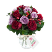 A luxurious, rounded bouquet of freshly opened roses, their petals unfurling in a lush conversation of deep crimson, burgundy and soft lavender hues. The arrangement reads like a velvet evening: rich red roses with velvety throats are balanced by pale lilac and dusty purple roses that soften the composition and lend a quiet, romantic glow. Dark, glossy greenery - the familiar Arrow-shaped leaves of Ruscus or Salal - nestles between the blooms, giving the bouquet depth and a cool, green perfume that grounds the sweeter rose scent. Scattered throughout, small red-orange rose hips or berry clusters add rustic punctuation, their firm, glossy skins catching light and introducing a lively texture against the petals' satin. The flowers sit in an antique-effect mercury glass vase, rounded at the base and narrowing at the neck, its silvered surface mottled and reflective so that each bloom and leaf shimmers when light moves across it; a simple natural twine is tied around the vase's neck, finishing the piece with an artisan's touch. A small rectangular white gift tag hangs forward from the twine, blank of any overt branding here, inviting a handwritten note to the recipient. Photographed against a clean white background, the bouquet's colours and reflective vase stand out with crisp clarity, suggesting freshness, thoughtful care and an occasion of quiet elegance. As a Gerrards Cross florist might arrange for an anniversary or intimate celebration, this bouquet feels both decadent and sincere - a floral message of admiration, comfort or tender congratulations delivered with steady craft and attention to texture, scent and colour.