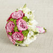 Laid gently on a pale, linen-like cloth, this bridal bouquet looks as if it has just been set down by a bride stepping out of a classic church in Gerrards Cross. The roses are the first thing to catch the eye: large, velvety blooms whose petals deepen from a soft, powder pink at the core to more vibrant fuchsia tones at the outer edges, creating a rich sense of depth and romance. Tucked snugly among them, clusters of lime green button chrysanthemums form small, rounded domes, their tightly packed florets offering a cheerful, almost tactile texture that recalls the fresh, bright greens of nearby Bulstrode Park after rain. Flowing along one side and circling the arrangement, delicate white lisianthus flowers open in loose, ruffled layers, mingling fully opened blooms with slender buds that tilt gently outward. Their creamy white and pure ivory tones introduce an ethereal, cloud-like softness that balances the bold pinks and greens. The stems underneath are gathered with precision and wrapped into a smooth handle, swathed in blush satin ribbon that feels quietly luxurious. Around this, strands of white pearls spiral and overlap, catching the light in a way that suggests heirloom jewellery or a treasured family detail added to the bridal flowers. Set against the understated beige background, the colours and textures of the bouquet stand out clearly without ever feeling loud, evoking calm joy and refined celebration. Crafted with the care of a local florist who understands Gerrards Cross weddings, this arrangement feels perfect for a ceremony followed by a reception in a nearby country house, delivering both beauty and meaning in every petal.