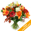 A vibrant, hand-tied autumn bouquet set against a clear white backdrop, composed with the confidence of an experienced florist. The arrangement centres on wide, trumpet-shaped orange lilies - their open petals and prominent stamens creating a warm, dramatic focal point - alongside a scatter of closed lily buds that promise more blooms to come. Rich, ruby-red and bright orange Gerbera daisies ring the lilies, their dense, circular petals offering cheerful contrast and a graphic rhythm. Creamy white Lisianthus with soft, ruffled edges add a cooling, tactile softness, while star-like Astrantia with purple-pink centres and fine, lacy bracts introduce a delicate, almost whimsical texture. Deep green foliage, likely ruscus or salal, nests the blooms and gives the composition a glossy, verdant base; throughout, deeply lobed oak leaves in burnt orange and reddish-brown are artfully interwoven, their crisp autumn tones anchoring the seasonal theme. The stems are gathered tightly and secured with dark twine or raffia, the traditional hand-tied finish visible where cut stems meet. The lighting is even and bright, revealing petal textures and the slight sheen of fresh leaves, and a faint, spicy, green scent seems to hang from the blooms. This bouquet reads as a cordial, autumnal embrace - suitable for a Thanksgiving table, a fall birthday, or a thoughtful doorstep surprise in Gerrards Cross near Packhorse Road or the station. In the lower right corner, a diagonal orange banner is superimposed on the image, clearly showing the white capitalised text FREE CHOCOLATE, a visual note of a seasonal promotion accompanying the floral photograph.