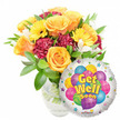 A vibrant, uplifting Get Well Soon arrangement set against a clean white backdrop, composed to comfort and brighten a recovery space. Large, velvety roses in warm orange and deep golden yellow form the heart of the bouquet, each petal unfurling in soft spirals that suggest gentle warmth and renewal. Sun-bright yellow gerbera daisies fan through the roses, their broad faces and darker centers catching soft daylight and introducing an immediate, sunny optimism. Deep burgundy and maroon carnations add plush, ruffled texture and visual depth, their denser petals contrasting with the smoother rose surfaces, while delicate sprays of white alstroemeria peek between the larger blooms, their fine petals and subtle markings lending a light, airy touch and a whisper of sweetness. A generous sweep of glossy green foliage frames and cradles the flowers, leaves of varied shape and sheen giving the arrangement a lush, garden-fresh feeling; through the clear glass vase the stems and water are visible, underscoring the bouquet's freshness and professional conditioning. Nestled to the lower right and slightly overlapping the blooms is a reflective round silver Mylar balloon, its surface decorated with a playful cluster of cartoon-style balloons in blue, purple, pink, yellow and green - some striped, some dotted - and cheerful yellow-and-blue lettering that reads get well soon. Small colourful starbursts pepper the balloon border and a tiny KALEIDOSCOPE logo sits at the very bottom edge. As a local florist might describe it for someone choosing a hospital or home delivery near Gerrards Cross High Street, the pairing feels thoughtfully crafted to send warmth, hope and a quick return to health.