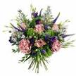 Against a clean white background, this hand-tied bouquet seems to glow with the gentle light of a late spring morning in Gerrards Cross. The first impression is one of softness and romance: full, layered roses in blush pink and muted mauve unfold in varying stages of bloom, some still shy and half-closed, others open enough to reveal the intricate pattern of their spiralled centres. Intertwined with them are plush, frilled carnations in dusty rose and purple-mauve, giving a tactile richness, as if each petal has been carefully ruffled by hand. Rising above the rounded shape, slender spires of deep violet Veronica stretch upward, adding height, structure, and a touch of drama that echoes the upright stems you might notice in the borders of local gardens near West Common. Threaded throughout are sprays of petite, daisy-like flowers in lavender and soft periwinkle, their yellow eyes brightening the bouquet and creating a sense of lightness and movement. Darker purple lisianthus blooms, with gently cupped petals, nestle between the softer shades, drawing the gaze deeper into the arrangement and lending it a luxurious, almost velvety quality. An abundance of foliage surrounds and supports the flowers: silvery eucalyptus leaves, lively lime-green textured filler, and softer greens that curl naturally around the edges, giving the bouquet a fresh, garden-picked feel. The stems beneath are neatly gathered and clearly hand-tied, suggesting the confident touch of a skilled local florist, ready for same-day delivery to homes and offices around Gerrards Cross, Chalfont St Peter, or a cosy café near the common. The overall mood is one of quiet celebration and heartfelt thoughtfulness, suitable for birthdays, anniversaries, or simply brightening someone's day.