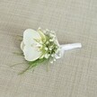 A delicately crafted white orchid boutonniere rests on a softly textured, light beige woven fabric, the kind of natural linen you might find in an elegant Gerrards Cross townhouse near East Common. At the heart of the design sits a pristine Phalaenopsis orchid bloom, its broad white petals gently curving outward with a subtle, satin-like sheen that catches the light. In the centre of the flower, the throat reveals a whisper of pale yellow and cream, adding gentle warmth and depth to the otherwise cool, clean white. Encircling the orchid are airy clusters of baby's breath, each tiny white Gypsophila flower forming part of a cloud-like halo that softens the silhouette and adds an ethereal, romantic quality. Fine, feathery strands of fresh green foliage, reminiscent of delicate fern fronds, peek out from beneath the blooms, providing a lively contrast of colour and a sense of natural movement, as if just gathered from a shaded garden off Packhorse Road. The stems are neatly aligned and expertly wrapped in a smooth white satin ribbon, tied into a small, understated bow that speaks of careful craftsmanship and attention to detail. The neutral oatmeal-coloured background gently frames the boutonniere without distraction, allowing the white petals and vivid greenery to stand out. The mood of the image is calm, poised, and timeless, ideal for a groom or groomsman at a Gerrards Cross wedding, perhaps in a local church or country house venue. It evokes the quiet excitement of a wedding morning, when each floral detail is carefully pinned in place, ready to accompany cherished vows and lasting memories.