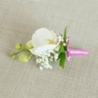 A delicate orchid boutonniere is laid horizontally on a soft, oatmeal-coloured linen background, its texture gently woven and quietly echoing the refined charm of a Gerrards Cross wedding. At the heart of this small floral piece is a single white Phalaenopsis orchid, its broad petals velvety and luminous, opening in a calm, symmetrical curve. The centre of the orchid reveals intricate detail: a soft wash of pale yellow and the faintest touch of pink around the throat, like a whisper of colour held close. Around the base, tiny clusters of white baby's breath gather in airy clouds, their fine, bead-like blossoms adding volume without disturbing the design's sense of calm. A few slender, bright green leaves peep from beneath the flowers, introducing a fresh, garden-picked contrast that feels at home in the leafy streets around East Common or West Common. Off to one side, several lime-green orchid buds remain tightly closed, suggesting new blooms to come and adding a quiet feeling of anticipation. The stems are neatly bound with a bright fuchsia satin ribbon, tied into a precise, miniature bow whose sheen catches the light and provides a joyful pop of colour against the neutral fabric. The lighting is soft and even, as though filtered through a window on a still morning, highlighting each petal edge and the subtle grain of the linen. This boutonniere feels ideal for a groom or prom guest stepping out in Gerrards Cross, carrying with them a touch of refined, contemporary elegance and the gentle scent of fresh flowers prepared with care by a local florist.