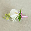 A refined wedding boutonniere is shown lying on a subtly textured, oatmeal-coloured linen surface, the understated backdrop echoing the natural elegance often seen at intimate celebrations around Gerrards Cross. The central flower is a flawless white Phalaenopsis orchid, its broad petals silky and gently arched, forming a graceful, open cup around a throat brushed with soft yellow-orange and the faintest hint of pink. This delicate colour at the centre feels like a quiet glow, drawing the eye inward. Around the orchid, wisps of white Gypsophila-baby's breath-cluster in airy sprays, each tiny blossom adding a cloud-like softness that enhances the orchid's sculptural form. Sleek, narrow green leaves are tucked thoughtfully through the design, their fresh colour adding structure and a lively contrast to the white blooms. Extending to one side, a slim stem carries three rounded orchid buds in pale green, still closed and full of promise, symbolising the unfolding of new chapters in life. The base is expertly bound in a bright pink satin ribbon, the fabric smooth and lustrous, tied into a neat bow with short, precise tails that lend a playful yet polished finish. The lighting appears gentle and diffuse, as if from a nearby window in a Gerrards Cross home, highlighting the subtle sheen of the petals and ribbon without harsh shadows. This buttonhole feels ideal for a groom, prom date, or special guest, the kind of piece that would be handcrafted by an experienced florist at Flower Delivery Gerrards Cross, then carefully pinned to a lapel to add a quiet, romantic accent to a tailored suit.
