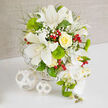 On a clean white tabletop framed by a soft beige backdrop, a lavish floral arrangement captures the calm elegance of a Gerrards Cross wedding reception. The bouquet is dominated by pure whites and fresh greens, lifted by hints of lemony yellow and glowing red. Several striking white Oriental lilies open generously, their smooth petals gently curving back to reveal speckled throats and pollen-tipped stamens that add subtle drama. Nestled among them, a creamy yellow rose spirals tightly at the centre, its velvety petals layered like folded silk. Surrounding these stars, airy sprays of white baby's breath drift between stems, softening edges and lending the impression of light morning mist over nearby Welders Lane gardens. Rounded tufts of vivid green Green Trick dianthus introduce a fun, mossy texture, contrasting with slender, feathery foliage that stretches outward to create a sense of effortless movement. Red hypericum berries gleam against the greenery, scattered like tiny jewels that bring a festive spark to the otherwise serene palette. Flowing down the right-hand side, a graceful cascade of white Phalaenopsis orchids tumbles from the main body of the design, each bloom pristine and symmetrical, with warm yellow centres and a few tender green buds yet to open. The bouquet is anchored in a subtle white woven basket, whose natural texture is reflected by two matching wicker spheres placed to the left on the table, suggesting thoughtful styling for a top table or entrance display. The gentle natural lighting and harmonious colours evoke a feeling of quiet celebration, ideal for couples planning sophisticated ceremonies and same-day flower delivery across Gerrards Cross and the surrounding villages.