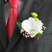 Pinned neatly to a tailored black jacket, this wedding boutonnière captures the refined charm so many couples in Gerrards Cross seek for their big day. A single white orchid forms the heart of the design, its petals thick and velvety, shaped into a graceful curve that feels sculpted rather than simply grown. Subtle hints of cream and soft yellow appear at the orchid's centre, adding warmth and depth when seen up close. Behind it sit two lime-green button chrysanthemums, their rounded, cushion-like blooms providing a playful contrast in both colour and texture, reminiscent of the fresh, lively greens in the gardens around West Common. Tiny clusters of baby's breath spill softly around the orchid, their cloud of tiny white flowers giving the composition a light, airy edge, like a gentle mist against the structured fabric of the suit. Deep green leaves frame the piece, adding structure and a natural backdrop that keeps the bright blooms from feeling too stark. At the base, the stems are bound tightly with a deep red ribbon, echoing the sheen of the red tie and introducing a subtle thread of romance. The gentle interplay of white, green, and crimson feels particularly suited to a wedding ceremony in a local church or a stylish reception nearby. From a florist's perspective, the piece showcases deliberate craftsmanship-the way textures balance, how colours converse, and how the boutonnière enhances the wearer without overpowering the overall look. It is a quietly confident detail, the kind that lingers in memory long after the last guests leave.