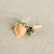 Presented against a soft, taupe-ecru weave, this buttonhole feels like a whisper of summer captured in miniature. The composition centers on a single apricot-peach rose whose petals unfurl in measured spirals, graduating from a warm, sunlit core to creamier, blushed edges; the surface of each petal reads velvet-smooth and faintly luminous under a gentle, natural light. Clusters of tiny white gypsophila sit like luminous breath beside the rose, their minuscule blooms creating a feathery halo that lends a sense of lightness and old-fashioned grace. Two rolled, glossy green leaves peek out behind the head of the bloom, their darker tone and curled form adding an elegant architectural curve, while slender bright-green grass blades introduce a fresh, lively rhythm to the silhouette. The stems are meticulously bound with a matching peach satin ribbon, tied in a discreet bow whose lustre mirrors the rose and invites one to imagine the tactile, satiny feel beneath the fingers. A fine silver pin is visible at the base - practical, restrained, and perfectly placed to fasten the piece to a lapel. Resting on the textured fabric, the boutonniere reads as both refined and tender, suited to intimate weddings, spring dances, or thoughtful gifts. If you're planning a ceremony in or near Gerrards Cross or a reception at a nearby hall in Beaconsfield or Denham, this design brings a quiet, romantic accent and the assurance of handcrafted floral expertise.