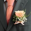 Suffused with understated elegance, this traditional boutonniere arrangement brings the romance of Gerrards Cross weddings vividly to life. The image captures the upper half of a gentleman's formal attire-a tailored slate-grey suit, its fabric playing softly with the light, forms the foundation. At the heart of the composition sits a blush-peach rose, its petals buttery and luminous, drawing gentle attention in the way wild roses bloom along Fulmer Common Road. Flanking the central rose, delicate white baby's breath weaves a frothy, cloud-like border, recalling morning mist on Denham Country Park's meadows. Graceful, verdant foliage arcs upward, infusing the design with lively movement and freshness, a nod to the natural beauty that frames Gerrards Cross. At the base, a sleek satin bow in peach softly gleams, echoing the colour of the expertly tied tie beneath. The effect is polished yet warm-a fragrance of summer gardens, a token of unity carefully crafted by local hands. More than a floral detail, this boutonniere serves as a quiet celebration of togetherness and joy, designed to be worn close to the heart as memories are created just steps from East Common's leafy walks.