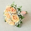 This captivating bouquet, lying across a softly woven beige linen, epitomizes romance with its lavish cluster of peach and apricot roses-each bloom revealing layers of delicate, unfurling petals, reminiscent of the gentle tones found in Gerrards Cross's summer gardens. Plumes of white baby's breath drift between the roses, lending an airy, cloudlike feel that lightens the lushness of the composition. The bouquet's circular form is balanced by flashes of deep green rose leaves, adding a sense of depth and natural vibrancy, similar to the wooded avenues near West Common. Securely wrapped in a coral-toned satin ribbon, the stems are finished with a spiral of tiny white pearls, offering a touch of refinement and bridal grace. Beneath the wrap, freshly cut stems peek out, reflecting careful attention to freshness and presentation. Soft, natural light bathes the bouquet, illuminating the subtle play of texture and hue in each floral layer. Crafted with the expertise of a local Gerrards Cross florist, this arrangement is perfect as a bridesmaid's bouquet or an elegant gesture for celebrations across the area. The overall effect is one of gentle sophistication and enduring festivity, echoing both the beauty of local tradition and the promises made on a special occasion.