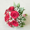 A romantic bouquet of red roses and baby's breath is captured resting on an understated off-white fabric, the kind of simple, elegant textile you might see on a wedding table in a charming Gerrards Cross venue. At the centre, a compact cluster of six to seven deep red roses forms the soul of the arrangement. Each rose is fully open but still holds a gentle cup shape, with layers of velvety petals curling outwards in lush spirals, suggesting passion, warmth, and a softly spoken declaration of love. Around these ruby blooms, an airy halo of gypsophila-baby's breath-creates a cloud of fine white blossoms. The tiny flowers are so numerous they seem almost mist-like, filling the spaces between each rose, lightening the composition and lending it a dreamy softness. Dark green leaves, polished and slightly pointed at the tips, peek from behind the blooms, giving the bouquet structure and a natural frame, much like the leafy trees along Packhorse Road frame the high street. The stems are firmly tied and carefully finished with a deep red ribbon that winds around the handle, embellished with a neat spiral of small white pearl-style dots. This subtle detail catches the light and gives a hint of jewellery-like sparkle, making the bouquet feel especially suited for wedding processions, engagement celebrations, or anniversary dinners at home. The whole piece, thoughtfully composed and beautifully balanced, carries the quiet luxury and intimate charm that couples in Gerrards Cross often seek for their most meaningful moments.