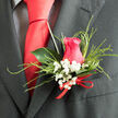Pinned carefully to a charcoal suit jacket, this romantic boutonnière showcases the refined craft of a local Gerrards Cross florist. A single hot pink rose takes centre stage, its petals rich in colour and softly layered, forming a perfect cup that suggests both strength and tenderness. Nestled closely around it is a halo of white baby's breath, the tiny star-like flowers creating a delicate mist that lightens the composition and evokes the soft fragrance of a garden border after rain on West Common. Wisps of fine, looping green grass encircle the rosehead, their arcs adding rhythm and grace, while a backdrop of dark, glossy green leaves grounds the piece and gives it a sculpted silhouette against the suit fabric. At the base, a slim scarlet ribbon is tied in a precise bow, the red tone echoing the warmth of the rose and signalling a special occasion-perhaps a wedding at a nearby country house or a formal celebration in town. The textures are varied yet harmonious: the velvety rose, the airy gypsophila, the smooth, almost waxy foliage, and the softly gleaming ribbon. Together, they create a compact design that feels both modern and rooted in classic tradition. Seen up close, this boutonnière speaks of care, intention, and the reassuring touch of a florist who understands how a single flower on a lapel can carry memories of vows, photographs on Packhorse Road, and the joy of being dressed just right for a once-in-a-lifetime day.
