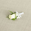 In this close-up image, a refined wedding boutonnière lies on a pale, woven fabric that resembles the gentle texture of linen, its understated backdrop echoing the calm streets and green spaces of Gerrards Cross. At the centre, a single ivory rose opens with quiet grace, its layered petals forming a soft spiral that draws the eye inward. The colour is a warm, creamy white, suggesting purity and romance without ever feeling stark. Clustered around the rose, tiny blooms of white gypsophila, commonly known as baby's breath, create a lacy cloud that lightens the design and adds a sense of airiness. Threaded through and around the flowers, thin blades of vivid green grass loop and curve, bringing a fresh, organic touch that feels as though it could have been gathered from a sunlit garden near West Common. The stems are wrapped with immaculate white satin ribbon, wound firmly yet smoothly so that no stray ends show, finished with a delicate, unfussy bow that hints at experienced craftsmanship. Soft, natural lighting accentuates the satin's gentle sheen and the velvety surface of the rose without casting harsh shadows. You can almost sense the cool, dewy freshness of the petals and the barely-there fragrance that would linger as this piece is pinned to a lapel before a ceremony at a local hotel or family gathering at home. The overall mood is one of quiet celebration and personal sentiment, the kind of classic boutonnière chosen by couples who value timeless style and thoughtful detail on their wedding day.
