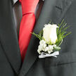 A close look at this wedding boutonniere reveals the kind of understated elegance that never goes out of style, the sort of detail often chosen for thoughtful ceremonies in Gerrards Cross. At its heart sits a single ivory-white rose, its petals smooth, velvety, and gently unfurling as if caught between promise and full bloom. The light catches along the outer edges, creating a soft glow against the charcoal fabric of a well-cut suit jacket. Cushioned around the base of the rose are dainty tufts of baby's breath, their tiny, star-like flowers forming a halo of softness that contrasts beautifully with the sharper lines of the lapel. Threaded between them are slim fern fronds and slender arcs of polished greenery, adding dimension, freshness, and a hint of wild garden charm reminiscent of the greenery around Gerrards Cross Common or the tree-lined avenues off Packhorse Road. At the bottom, a neat white ribbon bow wraps the stems, its satin finish reflecting just a touch of light and signalling care, tradition, and attention to detail. The boutonniere appears firmly secured in the breast pocket, sitting just above the stitching of the suit, as though ready to accompany its wearer down the aisle of a local church or into a celebration at a nearby hotel. The mood is calm and poised, with an undercurrent of excitement - a floral accent that quietly speaks of love, commitment, and the special moments shared with family and friends on an important day.