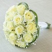 A beautifully detailed, close-up view captures the essence of a classic bridal bouquet, artfully arranged by a skilled florist in Gerrards Cross. The central focus is an opulent cluster of approximately twelve to sixteen creamy white and pale yellow roses, their petals delicately layered and at various stages of soft bloom, exuding a sense of purity and new beginnings. Intertwined among these blooms is an abundance of tiny, cloud-like white baby's breath flowers, lending an airy, almost weightless feeling to the composition. Swirling elegantly around the bouquet, slender ribbons of deep green bear grass contrast against the softness of the pale flowers, introducing an element of modern style and gentle movement reminiscent of walks along Fulmer Common Road. The bouquet's sturdy stems are neatly bundled and bound with luxurious white satin ribbon, forming a pristine handle that's both stylish and comfortable. Set against a light cream fabric background-perhaps echoing the tranquil interiors of a local events venue-the arrangement shines as an emblem of timeless romance and sophistication. Each detail, from the fresh, lightly fragrant roses to the balanced addition of filler and foliage, contributes to an atmosphere of refined celebration-making this bouquet ideal for weddings, anniversaries, or any moment in Gerrards Cross where heartfelt beauty is cherished.