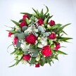 Photographed from directly above against a clean white background, this abundant hand-tied bouquet forms a full, almost perfectly round cluster of colour and texture. At its centre, velvety red roses in various stages of opening anchor the design, some still gently furled, others unfolding their layered petals in rich crimson tones that suggest romance and heartfelt affection. Close beside them, ruffled carnations in vibrant fuchsia and deep ruby red create a frill of soft, feathery petals, giving the arrangement a lively, celebratory energy. Nestled between the bolder blooms, clusters of dainty white spray chrysanthemums and other small, daisy-like flowers introduce a crisp, cool brightness, their neat little faces echoing the clarity of the white backdrop. Wisps of delicate white gypsophila-tiny baby's breath blossoms-thread lightly through the bouquet, appearing like a mist or fine lace laid over the stronger shapes. Around the edges, broad, pointed dark green leaves, likely from lilies or alstroemeria stems, provide structure and a glossy framework, while rounded, silvery-green eucalyptus leaves weave through the design in soft arcs, adding a contemporary flair and hinting at a fresh, herbal scent. The natural daylight in the photo highlights every detail without harsh shadows, making the reds appear rich and true, the whites fresh, and the greens deeply soothing. Crafted in the style you might find from an experienced Gerrards Cross florist preparing a special gift for a home near Austenwood Common or along Packhorse Road, this bouquet feels ideal for marking anniversaries, birthdays, or simple moments of gratitude, radiating warmth, joy, and an inviting sense of celebration.