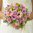This bouquet appears as though it has been gathered from a private garden tucked behind one of the elegant homes near East Common in Gerrards Cross, then refined by an expert florist's hand. The central roses, in shades of lilac and dusky mauve, open in precise spirals, each petal smooth and cool, carrying a quiet sense of grace and unspoken affection. Around them, feathery sprays of white gypsophila weave through the design like a soft mist, blurring any harsh lines and giving the eye a place to rest. Nestled amongst this softness, vivid green button chrysanthemums add a sparkling jolt of colour and texture, their compact, cushion-like blooms bringing a cheerful, modern twist. Curving through the bouquet, pink alstroemeria stems offer an elegant sweep, their long, narrow petals streaked with subtle markings that hint at gold and deeper rose, like brushstrokes across a pastel canvas. A collar of glossy greenery completes the arrangement, the leaves providing depth, structure, and a natural frame that makes the blooms appear to glow in the gentle daylight. The overall shape feels thoughtfully balanced-full yet airy, generous without being overwhelming-ideal for a bride walking down the aisle at a local church or intimate venue in Gerrards Cross. Imagine the bouquet held close, the textures shifting gently with each step, the colours harmonising into a soft symphony of romance and promise. Every detail, from stem length to petal placement, speaks to craftsmanship, care, and a deep understanding of how flowers can hold memory and meaning.