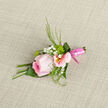 This image captures a finely crafted wedding boutonniere resting on softly textured fabric, its focal point a fully formed pink rose that seems to glow from within. The rose is tinted with a gentle gradient of colour, from a pale, almost ivory centre to richer pink edges, each velvety petal slightly curved and edged with a natural softness. Nestled alongside are pale pink alstroemeria blooms, their trumpet-shaped petals adorned with faint stripes and golden centres, bringing a sense of movement and lightness to the design. Delicate sprays of white baby's breath peek through the spaces, like tiny snowflakes suspended in air, giving the piece a romantic, airy quality that would feel at home at a wedding near East Common or a celebration close to Gerrards Cross station. Fine green foliage, including slender blades and soft sprigs, surrounds the blossoms, adding contrast and a cool, garden-fresh feel, as if the flowers have just been gathered from a nearby Buckinghamshire hedgerow. The stems are carefully aligned and wrapped in a smooth pink satin ribbon, wound tightly and finished with precision, suggesting the meticulous hands of an expert florist in Gerrards Cross. Gentle lighting highlights the glossy ribbon and the natural texture of each petal, creating a subtle play of shadows that emphasizes the arrangement's depth. You can almost sense the cool touch of the ribbon and the velvety surface of the rose under your fingertips. Ideal for a groom, best man, or special guest, this boutonniere quietly expresses tenderness, celebration, and thoughtful attention to detail.