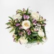 A compact, hand-tied bouquet is photographed from directly above against a spotless white background, so every blossom appears crisp, bright, and full of life. At the heart of the arrangement sit several creamy white and soft ivory roses, some still cupped in tight buds with a hint of buttery yellow at their core, others fully open to reveal spiralling layers of velvety petals. Threaded between the roses are alstroemeria, or Peruvian lilies, their slender buds and half-open blooms washed in gentle purplish-pink and lavender tones, with fine green streaks brushing their petals like watercolour. The contrast between the cool ivory and the mauve-berry shades gives the bouquet a refined yet romantic feel, reminiscent of a quiet walk through West Common in Gerrards Cross on a clear spring afternoon. Tiny star-like florets of white gypsophila, or baby's breath, form delicate clouds between the larger flowers, softening every edge and adding a light, airy movement. Beneath and around the blooms, a collar of deep, glossy green foliage folds and curves, creating a lush frame that anchors the composition and hints at the freshness of the stems beneath. The lighting is bright but gentle, with no harsh shadows, allowing each texture-from the satin-smooth rose petals to the feathery gypsophila-to be clearly defined. The bouquet feels elegant but approachable, the sort of arrangement a local Gerrards Cross family might send to celebrate a birthday, an anniversary at a favourite Packhorse Road café, or to offer quiet comfort. Every detail suggests the careful hand of an experienced florist who understands how colour, shape, and fragrance can create a moment of calm joy.