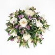 A top-down view reveals a lush, circular bouquet resting against a pure white background, where every flower seems to glow with quiet grace. At the heart of the design are creamy white roses, their petals spiralling from buttery ivory centres to softly ruffled edges, some fully open, others still gently cupped as if mid-breath. Woven among them are deep purple and dusky mauve Alstroemeria buds, their slender forms tipped with fresh green at the base, hinting at the streaked petals waiting to unfurl. Tiny clouds of white gypsophila drift through the arrangement, each spray of baby's breath adding a misty lightness that softens the richer tones. Dark, glossy foliage surrounds and supports the blooms, broad emerald leaves curving naturally to create a deep green cradle that makes the whites and purples stand out with striking clarity. The lighting is soft and even, like daylight filtering through a window on a calm afternoon in Gerrards Cross, revealing the velvet texture of rose petals and the slightly waxy sheen of the Alstroemeria. The overall impression is one of serene elegance and hopeful calm, the kind of bouquet you might send to a loved one on Packhorse Road or near West Common to offer comfort, quiet congratulations, or a thoughtful I'm thinking of you. Though the setting is minimal, the arrangement feels full of life and intention, as if freshly arranged by a local florist and placed before the camera at the very moment when every bloom is at its most beautiful and expressive.