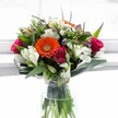 This exuberant bouquet encapsulates the fresh, welcoming spirit of Gerrards Cross, much like the first burst of colour in local springtime gardens. At its core, a radiant tangerine-orange Gerbera blooms with warmth and vitality, flanked by clusters of rich magenta and deep pink roses in both tightly furled buds and lush velvet petals, recalling the romantic charm found in hidden corners of Gerrards Cross's leafy avenues. Creamy white alstroemeria with their distinctively striped petals bring a graceful contrast, while delicate white chrysanthemums introduce a soft, lace-like layer that lightens the entire composition. Gentle hints of pale yellow and soft cream roses crown the bouquet, mingling with subtle sprays of lavender and purple hues for depth and surprise. Encircling all, broad glossy leaves and delicate green accents echo the flourishing greenery of local commons and parks, artfully supporting and shaping the arrangement. The crystal-clear cylindrical glass vase, filled with fresh water, showcases the preparation and dedication of local florists. Illuminated by natural daylight-evocative of a window overlooking West Common-the entire display glows, ready to brighten a birthday table, mark an anniversary, or serve as an elegant gesture delivered to homes and offices throughout Gerrards Cross.