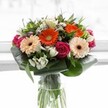A vivid celebration of floristry, this bouquet reflects the cheerful spirit found throughout Gerrards Cross. Four gerbera daisies command attention at the heart of the arrangement-two ablaze in bold orange, two softer and creamier, all with rich chocolate-hued centers that invite the gaze. Surrounding them are magenta roses, tightly furled in plush whorls, weaving a thread of elegance and romance through the design. Sprays of crisp white alstroemeria and sprightly white spray roses glimmer against the lush greenery, while light pink blooms and delicate white fillers add layer upon layer of inviting texture. Framing this abundance, lustrous paddle-shaped aspidistra leaves curve protectively around the base, fortified by slender pointed foliage that fills the spaces and adds movement. Presented in a tall, crystal-clear glass vase, every green stem is showcased, reinforcing a sense of fresh-cut vibrancy. The backdrop-a soft, sunlit glow suggestive of a calm morning in Gerrards Cross-accentuates the arrangement's colour and depth. Whether intended to mark a milestone, uplift a loved one, or serve as a centrepiece for gatherings near East Common, this bouquet is a heartfelt expression of local artistry and joy, radiating gratitude and warmth from every petal.