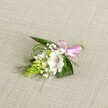 A delicately handcrafted boutonniere rests on a softly textured, light beige fabric, its surface reminiscent of natural linen laid out on a quiet morning in Gerrards Cross. At the heart of this small floral piece is a single white alstroemeria bloom, its broad, velvety petals opening gracefully to reveal fine reddish-brown speckles clustered toward the throat, like careful brushstrokes on porcelain. Just to the side, a compact cone of vivid lime-green buds, similar to an Ornithogalum spike, introduces a sculptural element, the buds tightly packed and glistening with freshness. Scattered throughout are airy tufts of white baby's breath, their tiny flowers floating like a soft mist around the central lily, creating a cloud-like halo that lightens the whole design. Supporting the flowers is a foundation of deep green, pointed leaves and slender, grass-like fronds that arc and weave through the piece, adding movement and a gentle sense of wildness, as if plucked from a garden near East Common. At the top edge of the boutonniere, a neat pink satin ribbon is tied into a small, precise bow, its glossy texture catching the light and adding a playful yet refined splash of colour. The even, natural lighting highlights every vein in the foliage and every speckle on the alstroemeria, conveying a feeling of careful craftsmanship and quiet celebration. This compact floral adornment feels perfect for a wedding lapel, prom night, or intimate celebration in Gerrards Cross, capturing the tenderness and anticipation of a special day with its soothing blend of white, green, and blush pink tones.