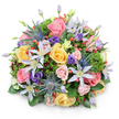 Set against a crisp white background, this lush, rounded bouquet looks like a carefully gathered piece of countryside brought indoors, its dome shape full and perfectly balanced. At the forefront are generous blooms of garden roses in shades of light pink, mellow yellow, and soft peach, each flower layered with ruffled petals that curl outward in graceful spirals. Some roses are fully open, showcasing their intricate centers, while others are still gently closed, adding a sense of freshness and quiet anticipation. Woven between them are delicate, star-shaped clematis blooms in white and pale lavender, their slender petals and golden-yellow centers lending a light, almost floating quality. Striking spikes of blue eryngium (sea holly) punctuate the pastel softness, their metallic blue-grey heads providing a modern, textural contrast. Deep purple lisianthus blooms, from small buds to softly unfolding flowers, contribute moody jewel tones that echo evening skies over Gerrards Cross Common. Scattered throughout, clusters of glossy red hypericum berries add tiny bursts of vivid colour and a pleasing roundness of form. The entire composition is cradled in a layered bed of greenery, including broad, shiny leaves at the base and finer, feather-like sprigs that fill any gaps, with occasional hints of darker, burgundy foliage tucked inside for depth. The lighting is even and bright, emphasizing the bouquet's freshness and the intricate interplay of shapes and textures. It feels like a hand-crafted arrangement ready to be delivered to a home on Packhorse Road or a celebration near the station, perfect for birthdays, thank-yous, or simply bringing a moment of joy into everyday life in Gerrards Cross, all while reflecting the thoughtful artistry of the local florist who arranged it.