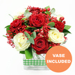 This image shows a lush, romantic rose arrangement captured against a simple white background, its colours and textures standing out with the clarity of a freshly arranged bouquet in a Gerrards Cross florist's studio. At the heart of the design, velvety deep red roses open into generous, layered blooms, each one rich in tone and emotion. Nestled between them, creamy white roses unfold in softer spirals, their gentler hue bringing balance and a sense of quiet elegance, like candlelight in a Denham Lane sitting room. Fine clusters of bright red filler flowers, reminiscent of tinted gypsophila, weave through the arrangement, adding an airy, cloud-like effect that lightens the overall look. Punctuating this softness, polished red hypericum berries sit in small clusters, their rounded, bead-like shapes and glossy finish catching the light and echoing the joyful feel of festive decorations along the Gerrards Cross high street. Around the roses, a mix of fresh greenery fans out-deep green leaves and slender sprigs of eucalyptus in cool blue-green tones-creating contrast, depth, and an imagined whisper of fresh, aromatic scent. The stems are gathered neatly into a modern, clear rectangular glass vase, where every stem can be seen crossing and rising, adding structural interest. Around the middle of the vase, a green and white gingham ribbon is wrapped with care, lending a cheerful, homely touch that would suit a kitchen table near West Common or a cosy corner by Bulstrode Park. In the lower right of the picture, an orange circular badge with crisp white text reads VASE INCLUDED, making it clear this is a complete, ready-to-display floral gift-perfect for birthdays, anniversaries, or sending love with same-day delivery throughout Gerrards Cross.