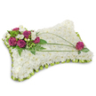 A rectangular pillow-shaped sympathy cushion, photographed against a crisp white background where a soft shadow anchors its gentle presence. The entire surface is a dense, cloud-like field of pristine white chrysanthemum florets, their tightly layered petals forming a velvety, textured plane that reads as pure, peaceful repose. Along the edge a neat scalloped trim of folded lime-green satin ribbon gives the pillow a subtle ruffled frame, the cool chartreuse tone breathing a quiet lift into the composition. In the upper left corner a compact spray of deep magenta roses-rich, velvety and fully open-sits amid delicate white freesia blooms, the freesias' slender trumpets and pale scent offering a delicate contrast to the roses' weight. Fresh green foliage, including feathery fern fronds and small glossy leaves, cradles the cluster and provides depth and a living backdrop. Two slender arcs of green linear foliage, likely bear grass, sweep across the white surface in a gentle diagonal, creating movement that guides the eye toward a single matching magenta rose placed thoughtfully near the lower right corner. The colors-pure white, vivid magenta and lime green-remain true and harmonious under soft studio light, which highlights petal texture and the satin's faint sheen without harsh shadows. This arrangement reads as a traditional, comforting floral pillow meant for a funeral or memorial, symbolising rest and remembrance; it feels like the kind of tribute a local Gerrards Cross florist might prepare for a service on the High Street or for delivery to the station chapels, offering a composed, tender expression of condolence and respect.