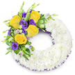 A delicate circular funeral wreath, carefully formed as a soft, cloud-like ring of tightly clustered white spray chrysanthemums, rests against a clean white background. The chrysanthemums are densely packed so their many narrow petals create a seamless, cushiony texture that reads as peaceful and pure; you can almost sense the faint, green-sweet scent of freshly cut blooms. Nestled into the upper left curve is an intentional, eye-catching spray: several fully opened yellow roses in buttery to golden tones, their spiralled petals offering a warm, gentle lift against the white base. Interwoven with the roses are deep purple lisianthus (Eustoma), their ruffled, cup-shaped blossoms and a few paler lavender buds providing cool colour contrast and a satin-like softness. Small unopened lisianthus buds and tender green shoots add depth and the impression of life continuing, while glossy rounded leaves, variegated greenery and delicate fern fronds give a verdant frame to the accent. A subtle dark purple mesh or crinoline ribbon peeks from beneath the chrysanthemums along the inner and outer edges, providing a refined echo of the purple blooms and a whisper of texture under the petals. The wreath's open centre and balanced composition read as dignified and consoling, suited to graveside tributes or a church memorial service in Gerrards Cross or nearby Stoke Poges. As a florist describing this piece, I imagine it carried through the quiet streets to a local service, a handcrafted emblem of comfort, purity and the quiet warmth of remembered light.