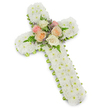 A traditional floral funeral cross, rich with texture and meaning, is pictured against a spotless white background, the soft drop shadow giving the impression that it hovers delicately in the light. The body of the cross is densely covered with small, perfectly formed white chrysanthemums, their button-like heads arranged so closely that they form a plush, continuous blanket of petals. This expanse of white feels peaceful and contemplative, the floral equivalent of a quiet prayer offered in one of the churches around Gerrards Cross. At the centre, where the upright meets the crossbar, a tender cluster of roses provides a gentle focal point. Fully opened blooms in muted tones of blush pink, ivory, and pale peach are gathered together, each rose layered with soft, spiralling petals that suggest affection and farewell. Threaded through these central flowers are wisps of pale lavender filler blossoms and slender green fern fronds, adding lightness, movement, and natural grace. Along the outer edge of the cross, a fine lime green ribbon traces the silhouette, just visible beneath the chrysanthemums and giving the shape a clear, defined border. This hint of green lifts the design, like the first buds of spring along a Gerrards Cross garden path, and symbolises quiet renewal amid sorrow. The overall effect is composed and deeply respectful, a lovingly made tribute that could rest near the coffin, at the front of a service, or by a graveside, offering a visible sign of faith, remembrance, and the lasting bond with the person who has passed.
