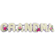 The image presents a beautifully composed funeral flower tribute that spells GRANDMA in large, comforting block letters. Each letter is entirely covered with pristine white chrysanthemums, arranged in a close, even layer that gives the surface a soft, pillowy look, like freshly fluffed cushions. A narrow lilac ribbon trims the outline of every letter, its pastel purple tone adding a gentle whisper of colour and framing the design with understated elegance. Positioned like little jewels, three small posies of mixed blooms bring a tender burst of life: bright pink gerbera daisies, petite pink roses, and a mix of fresh green foliage. These accent clusters are carefully set at the first G, the central A, and the last A, creating a pleasing visual rhythm across the word and suggesting cherished moments scattered through a lifetime. The lighting feels calm and diffused, revealing the natural textures of each petal and leaf without harsh contrast, as if the tribute were resting quietly in a Gerrards Cross chapel or at a graveside near the peaceful edges of the Common. There is an impression of fresh, clean fragrance-softly floral rather than overpowering-that might comfort mourners as they pass by. Crafted with the steady hands and empathetic heart of a local florist used to helping families say farewell, this arrangement speaks through its colour palette of white, lilac, and pink, offering both solace and gratitude. It captures the essence of a beloved grandmother: gentle, dependable, and warmly remembered, a floral embrace that continues even when words fall short.