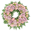 A meticulously crafted circular wreath rests flat on a pure white surface, its tidy outline and full composition evoking the feeling of a carefully prepared farewell, perhaps for a quiet service in Gerrards Cross or nearby Chalfont St Giles. The outer edge is formed by a thick band of dark, glossy fern fronds, their finely feathered leaves curving outward and overlapping in multiple layers, creating a deep, green cushion that frames the flowers. Inside this green halo, the wreath is crowded with roses, every gap thoughtfully filled so that the arrangement looks plush and abundant. The main flowers are large, fully open roses, petals arranged in delicate spirals of dusty lavender, muted mauve, and grey-tinged purple, a palette that feels both modern and timeless. Nestled among them, smaller clusters of blush pink spray roses and petite rosebuds add softness; some blossoms are just beginning to open, suggesting new memories even as they honour those already past. Discreet accents of darker greenery and tiny buds are tucked between the roses, introducing subtle shadows and a sense of layered depth. The lighting is bright yet gentle, making the pastel tones appear clear and true while allowing the greens to remain rich and saturated. The overall effect is one of calm, understated elegance: a wreath that speaks quietly of love, gratitude, and respect. It would be a fitting tribute for a funeral, memorial, or graveside visit in the Gerrards Cross area, reflecting the care and sensitivity of an experienced local florist who understands how flowers can offer comfort when words feel difficult.