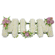 A tender, three-dimensional funeral tribute spells the word 'MOM' in bold capital letters, each letter built from hundreds of small, tightly packed white chrysanthemums that give the surface a soft, cloud-like texture. The flawless white of the sprays reads as quiet and pure in the soft studio light, suggesting calm and reverence; the chrysanthemums' faint green, herbaceous scent would be barely perceptible but grounding. To soften the austerity, three small clusters of pastel blooms-muted lavender roses and gentle blush-pink rosebuds-are artfully placed: one on the upper left curve of the first 'M', a smaller cluster cradled at the base of the central 'O', and a mirrored grouping on the upper right of the final 'M'. Sprays of fresh green foliage and delicate fern fronds tuck among the roses, adding cool, slender lines and depth against the white mass. A darker green structural band-possibly a ribbon-wrapped frame or mossed base-peeks beneath the blooms, anchoring the letters and giving them a unified, dignified silhouette. The arrangement reads as a calm, personal expression of love and remembrance, suitable for a funeral service, chapel display, or graveside committal. The composition is crafted with the careful touch of a seasoned florist: blooms tightly placed for lasting presentation, color accents balanced to carry the eye across the whole word, and foliage used sparingly to preserve the tribute's respectful simplicity. For families seeking a comforting, understated memorial in Gerrards Cross and nearby communities, this 'MOM' tribute offers a sincere, floral embrace for a farewell moment.