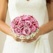 In the graceful quiet of a sunlit morning in Gerrards Cross, a bride clasps a hand-tied bouquet just beneath her lace-trimmed bodice-a moment of delicate anticipation before the vows. The bouquet itself is a poetic blend of artistic intention and emotion: roses, their petals unfurling from gentle, creamy-pink centers into boldly saturated magenta rims, create depth and allure, while clusters of white baby's breath weave through the composition like tufts of cloud drifting across blue skies over Austenwood Lane. The bride's hands, lovingly manicured and brushed with pale shimmer, hold the arrangement softly, as if cradling both memory and hope. Lacy floral patterns stretch across her sleeveless white gown, a V-neck adding understated elegance, and a flowing sash softly pools beside her wrists. Light spills across the bouquet, intensifying the interplay of colour and texture, as the neutral, blurred backdrop ensures the florals steal focus. Crafted with the refined touch and local knowledge honed by Gerrards Cross's finest florists, this bouquet encapsulates serenity, devotion, and the sweet anticipation that marks the beginning of every love story. A scene brimming with gentle promise, it tells a tale perfect for any wedding dreamed of beneath the heritage trees of Gerrards Cross.