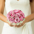 In this romantic bridal image, a tightly gathered dome of blush pink roses rests securely in the bride's hands, the bouquet poised against the intricate ivory lace of her wedding dress. Each rose is at the height of bloom, petals unfurling in soft, overlapping layers that create a sense of depth and luxury, from pale shell-pink at the edges to a richer blush at the heart. Threaded delicately between the roses, clusters of white gypsophila form a fine, cloud-like border, their tiny star-shaped flowers softening every contour of the arrangement. The overall impression is of a classic, hand-tied bouquet, serene and perfectly balanced, with barely a stem visible, just a glimpse of tender green at the base. The light feels natural and gentle, as if the bride is standing near the greenery of West Common or by a sunlit window in a Gerrards Cross venue, enhancing the subtle glimmer of lace and the natural sheen of each petal. There is a quiet sense of stillness and anticipation, as though captured moments before the walk down the aisle. Imagine the fragrance: warm, fresh rose notes drifting upwards with every breath, mingling with the airy, almost herbal crispness of the gypsophila. The way the bride's fingers curl gently around the handle suggests care and confidence, a woman fully present on her wedding day. As florists who work closely with couples in Gerrards Cross and the surrounding villages, we design bouquets like this to reflect not only romance but also a sense of place-elegant yet welcoming, much like the tree-lined streets and relaxed charm of the local community-perfect for same-day wedding flower delivery and last-minute finishing touches.