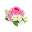 A compact, hand-crafted floral corsage rests against a pristine white backdrop, composed with the quiet confidence of an experienced florist. At its center sits a lush bubblegum-to-fuchsia pink rose, petals tightly spiralled in velvet layers that catch the soft studio light and suggest a warm, floral perfume. Encircling that focal rose are rounded clusters of hydrangea in whisper-soft pastel pink and a faint lavender wash, their tiny florets building airy volume and a romantic, cloud-like texture. Twin creamy white, trumpet-shaped blooms-reminiscent of small amaryllis or petite lilies-tilt gently forward, each with a greenish throat that introduces a fresh, verdant note to the palette. Beneath and between the blooms, broad deep-green leaves lend weight and contrast; their glossy surfaces reflect a hint of light and anchor the composition with garden-fresh depth. From one side rise slender, vibrant green buds with delicate yellow tips, adding upward movement and the promise of blooms to come. At the lower right a small cluster of luminous, off-white pearls is artfully draped, varying slightly in size to suggest heirloom jewellery and to heighten the arrangement's refined, bridal feel. The overall impression is one of intimate elegance-suitable for weddings, proms, anniversary corsages, or a thoughtful keepsake for spring and summer celebrations-where soft textures and a classic colour story convey love, tenderness, and timeless poise. The arrangement reads as both summer-garden freshness and formal sophistication, made to sit comfortably against bridal whites or a tailored suit at a local ceremony or reception.