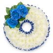 Photographed from above against a clean white backdrop, this bespoke funeral wreath is carefully formed into the number '0', a personalised tribute often chosen to mark an age or special number at a memorial. The entire numeral is covered in a plush, even layer of small white spray chrysanthemums; their tiny, tightly packed florets create a cloud-like surface that reads as both soft to the touch and visually calming, the petals catching a diffuse, gentle light that suggests a quiet morning service in Gerrards Cross. A fine, pleated royal blue satin ribbon traces both the outer and inner edges of the '0', its scalloped ruffling providing a crisp, dignified frame whose satin sheen picks up subtle highlights as the eye travels around the shape. Nestled along the upper-left curve, three vivid royal blue roses form the sole focal point-a deliberate, striking trio whose deep, velvety petals unfurl from firm centers and contrast beautifully with the chrysanthemum cushion. Small clusters of glossy dark green leaves sit behind the roses, offering depth and a whisper of woodland freshness reminiscent of nearby Beaconsfield copse or the hedgerows beyond Denham. The colour pairing-pure white and deep sapphire blue-reads as respect and serenity, a quiet nod to tradition that could also reference a uniform, club colours, or a dearly held favourite. The overall impression is meticulous, balanced and comforting, the craftsmanship suitable for church services, chapel viewings, or a graveside farewell in local churchyards around Packhorse Road and the town's leafy lanes. This arrangement communicates sympathy and steadfast remembrance through texture, colour and considered floral placement.