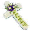 The image presents a refined cross-shaped floral tribute, designed with the kind of care you might expect from a local Gerrards Cross florist accustomed to intimate family funerals and memorials. The cross stands out clearly against a white background, its strong outline created by a continuous border of fresh, vivid green ribbon or neatly aligned foliage that traces every curve and angle. Within this border, the entire surface is filled with small, pristine white chrysanthemums, their petals packed tightly to form a soft, plush texture that evokes snow or a downy blanket, embodying peace, purity, and rest. A vertical panel of lime-green button chrysanthemums runs down the centre of the cross's upright stem, offering a rhythmic note of colour that feels hopeful and gently uplifting. Over this green section, very fine, pale wires are arranged in a loose criss-cross, adding a contemporary twist and a sense of hand-crafted detail. At the heart of the design, where the arms meet, sits a striking spray of deep purple lisianthus, their velvety, cup-shaped blooms contrasting dramatically with the surrounding white. These purple flowers are interspersed with more lime-green chrysanthemums, tying the colours together, while arching fern fronds in deep green curl softly around the cluster, creating depth and movement. The composition is calm and balanced, a classic Christian floral cross suitable for placing beside a coffin, at a chapel, or on a grave in the Gerrards Cross area, expressing condolences, remembrance, and quiet hope through its harmonious blend of white, green, and purple.