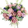A lavish, hand-tied bouquet rests against a clear white backdrop, every flower and leaf composed with the care of a seasoned Gerrards Cross florist. At its core, generously petalled garden roses open in shades of soft blush pink, dusty mauve, and antique rose, their velvety spirals suggesting tenderness and quiet romance. Around them, layers of frilled carnations swell outward, their ruffled petals blending from creamy ivory and blush at the centres into deeper pink and plum around the edges, creating a sense of movement, like ripples on the surface of Misbourne water nearby. Deep indigo blooms, resembling tight tulip or anemone buds, are strategically placed to punctuate the softer tones, while an open royal blue anemone with a dark, almost inky centre near the base of the bouquet becomes a dramatic focal point. Slender wands of pale lilac and lavender stock weave through the design, their many small blossoms adding a gentle vertical rhythm and a whisper of sweet, powdery fragrance. Embracing the flowers is a generous collar of foliage: rich, dark green rose leaves interlace with rounded, silvery eucalyptus, bringing cool contrast, texture, and a suggestion of fresh, clean aroma. The natural stems are visible and neatly tied at the bottom, underscoring the craftsmanship and indicating a bouquet ready to be delivered to a home or celebration across Gerrards Cross. The mood is both comforting and elegant, making this arrangement ideal for anniversaries, milestone birthdays, or sending a thoughtful message of care and admiration to someone nearby.