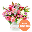 A generous, romantic bouquet bursts from a square glass vase, photographed against a pristine white backdrop that highlights every blossom and leaf. The arrangement is built around an array of pink roses, some in deep, almost jewel-toned fuchsia and magenta, others in soft, gentle blush, their velvety petals unfolding with classic elegance. Intermingled with these are plentiful carnations in coral and peach-pink, their ruffled petals giving the whole composition a plush, layered texture. Scattered between the larger blooms are small, daisy-like chrysanthemums in pretty lavender and purple shades, each with a vivid green centre that adds a refreshing brightness to the overall palette. Creamy white blooms provide visual rest, softening the stronger colours and making the pinks appear even richer. A generous selection of foliage frames the flowers: rounded eucalyptus leaves in a muted silvery-green tone contrast with darker green leaves, while a few reddish-brown sprigs suggest a whisper of autumn or a deep, romantic accent. The stems are gathered neatly into a clear glass vase with softly rounded edges, through which you can see the tidy cut stems. Around the base, a white band encircles the vase, printed with tiny red hearts and the tender message all my love, evoking a heartfelt gift that might be sent to a loved one living near Gerrards Cross Common or along Fulmer Road. In the bottom right corner of the image, an orange circular graphic with bold white capital lettering reads VASE INCLUDED, indicating that this is a complete, ready-to-display gift arrangement, ideal for local deliveries marking birthdays, anniversaries, Valentine's Day, or simple everyday appreciation in Gerrards Cross.