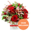 A dramatic yet refined floral arrangement in rich shades of red and soft pink is centred in the frame, placed in a clear glass vase against a bright white background that emphasises every nuance of colour and form. At its core, sumptuous velvety red roses, some just beginning to unfurl and others more fully open, express a sense of passion and tenderness, reminiscent of an intimate celebration at home after a walk through Gerrards Cross. These star blooms are interwoven with clusters of smaller deep crimson flowers, similar to alstroemeria, whose layered petals provide contrast and a gently ruffled texture. Throughout the bouquet, fine sprays of miniature pale pink and white flowers, much like waxflower, are scattered liberally, their tiny blossoms and buds adding a delicate, almost lacy overlay that breaks up the intensity of the reds. Encircling the flowers is an abundance of fresh greenery: broad, deep green leaves paired with lighter, more delicate foliage, giving the arrangement a full, rounded silhouette and a sense of natural lushness. Among the greens, carefully positioned burgundy and reddish-brown leaves with subtle veining lend depth and a slightly dramatic, autumnal note, complementing the roses without overpowering them. The entire composition is anchored in a sleek, rectangular glass vase, its clean lines and visible stems contributing a modern, polished feel that suits contemporary homes and offices around the Gerrards Cross area. A charming red ribbon, printed with neat white heart outlines, is tied around the vase, reinforcing the romantic theme and making the display feel truly gift-ready. In the bottom right corner of the image, a circular orange emblem clearly states VASE INCLUDED in bold white capitals, signalling that the arrangement arrives as pictured, ready for gifting on anniversaries, Valentine's Day, or any heartfelt occasion.