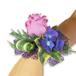 Perched gently on a fair-skinned wrist against a crisp white backdrop, this modern corsage reads as a small, wearable garden. At its center a partially open pink rose unfurls-petals soft as velvet, their color graduating from a pale candy pink toward edges brushed with a deeper magenta-inviting the eye and suggesting a faint, powdery rose scent. Nestled beside it, clusters of deep purple hydrangea provide a luxurious counterpoint; each tiny floret carries a subtle blue-tinged heart that seems to glow when turned in soft light, giving the cluster a rich, multi-dimensional look. The piece is framed with varied green textures: narrow, silvery-green sprigs (reminiscent of eucalyptus or dried lavender) that add a cool, aromatic note and fine feathering; glossy, variegated ivy leaves with dark green centers and creamy yellow margins that lend a classic, slightly formal edge; and a sculptural wide leaf striped in white and green, tightly curled into an elegant spiral for a contemporary flourish. Underpinning the blooms, an open-weave deep purple mesh peeks through, its lacy texture amplifying the hydrangeas' tones and adding a subtle, evening-ready shimmer. The florist's hand is clear in the balanced composition-colors and materials layered to create depth, movement, and tactile contrast. In Gerrards Cross this corsage would suit bridal parties stepping out from the High Street boutique or prom-goers leaving the station on an early summer evening. It reads as celebration and restraint at once: fresh, scented, and designed to sit comfortably against skin while drawing compliments and gentle, memorable attention.