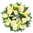 Viewed from above, a perfectly circular sympathy wreath lies flat against a clean white background, its dense construction giving an immediate sense of calm and measured care. At the heart of the design, fifteen to twenty creamy ivory roses open in soft, rosette spirals, their petal edges catching a cool, diffuse light that makes them appear almost luminous. Interspersed among the roses are pale lemon-yellow lilies; some trumpet-shaped blooms are fully unfurled, showing their slender stamens, while others rest in elegant bud form, offering gentle vertical notes and a promise of unfolding life. A rich bed of deep green foliage-feathery fern fronds that soften the wreath's silhouette and rounded sprigs of eucalyptus with their muted blue-green tones-frames and supports the flowers, creating layered depth and subtle contrast. The scent is suggested rather than overpowering: a faint powdery sweetness from the roses tempered by a green, slightly citrus edge from the lilies and eucalyptus, as if the wreath had been placed in the cool morning air outside a village chapel on Packhorse Road. The circular form reads as a deliberate symbol of continuity and remembrance; every bloom is set with respectful symmetry, the overall palette of cream, pale yellow, and verdant greens designed to convey peace, purity, and sincere condolence. As a florist with local experience around Gerrards Cross and nearby Beaconsfield, I picture this arrangement laid gently at a graveside or chapel table-an unobtrusive, comforting tribute that honors memory while promising quiet solace.